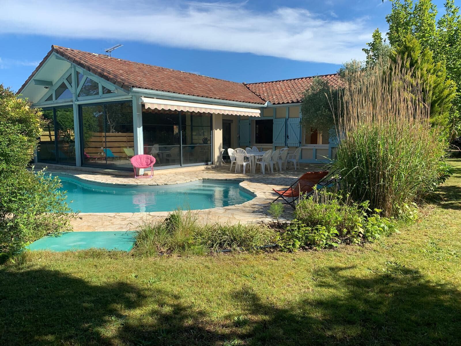 Une maison avec une piscine, un espace salon extérieur et une terrasse couverte.