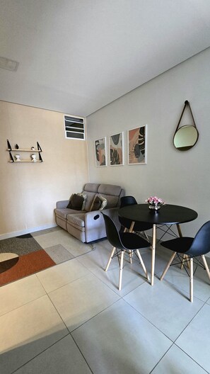 A living room with a sofa, a dining table with chairs, a hanging mirror, and wall art.