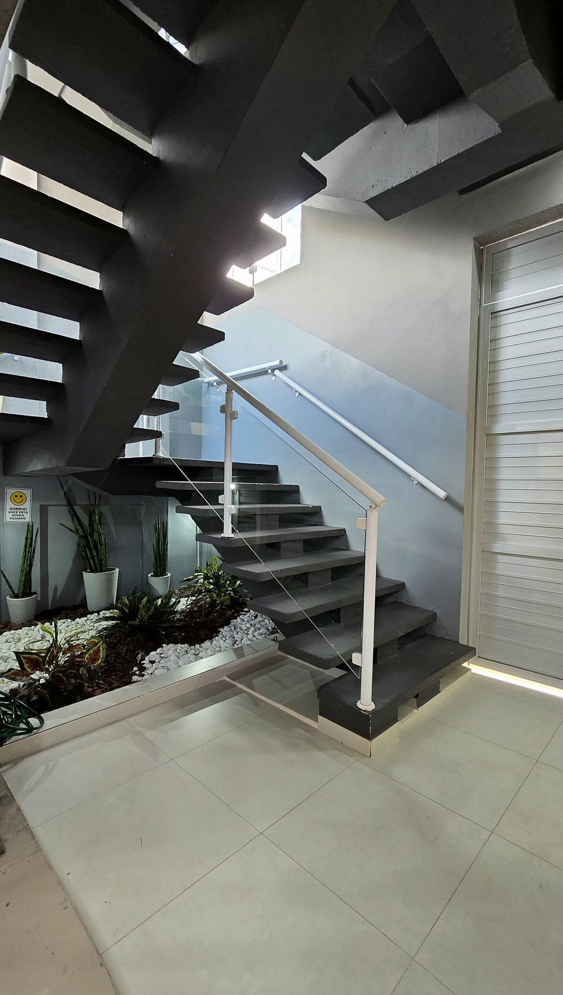 Uma escada moderna com guarda-corpo de vidro e corrimão de metal, que leva a um patamar com uma porta.