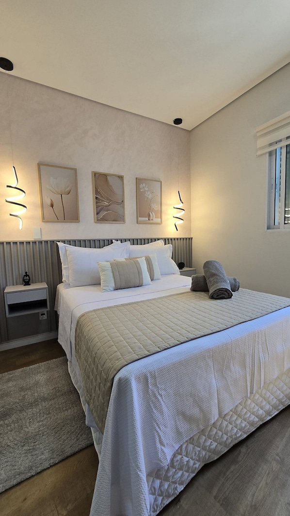 Un dormitorio moderno con una cama grande, una mesita de noche, una lámpara de pared y una ventana.