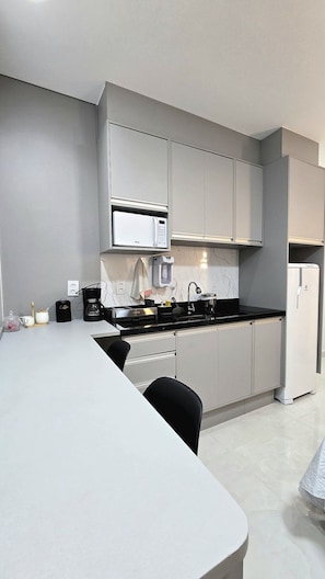 Una cocina moderna con armarios grises, horno empotrado, cafetera y un lavabo.