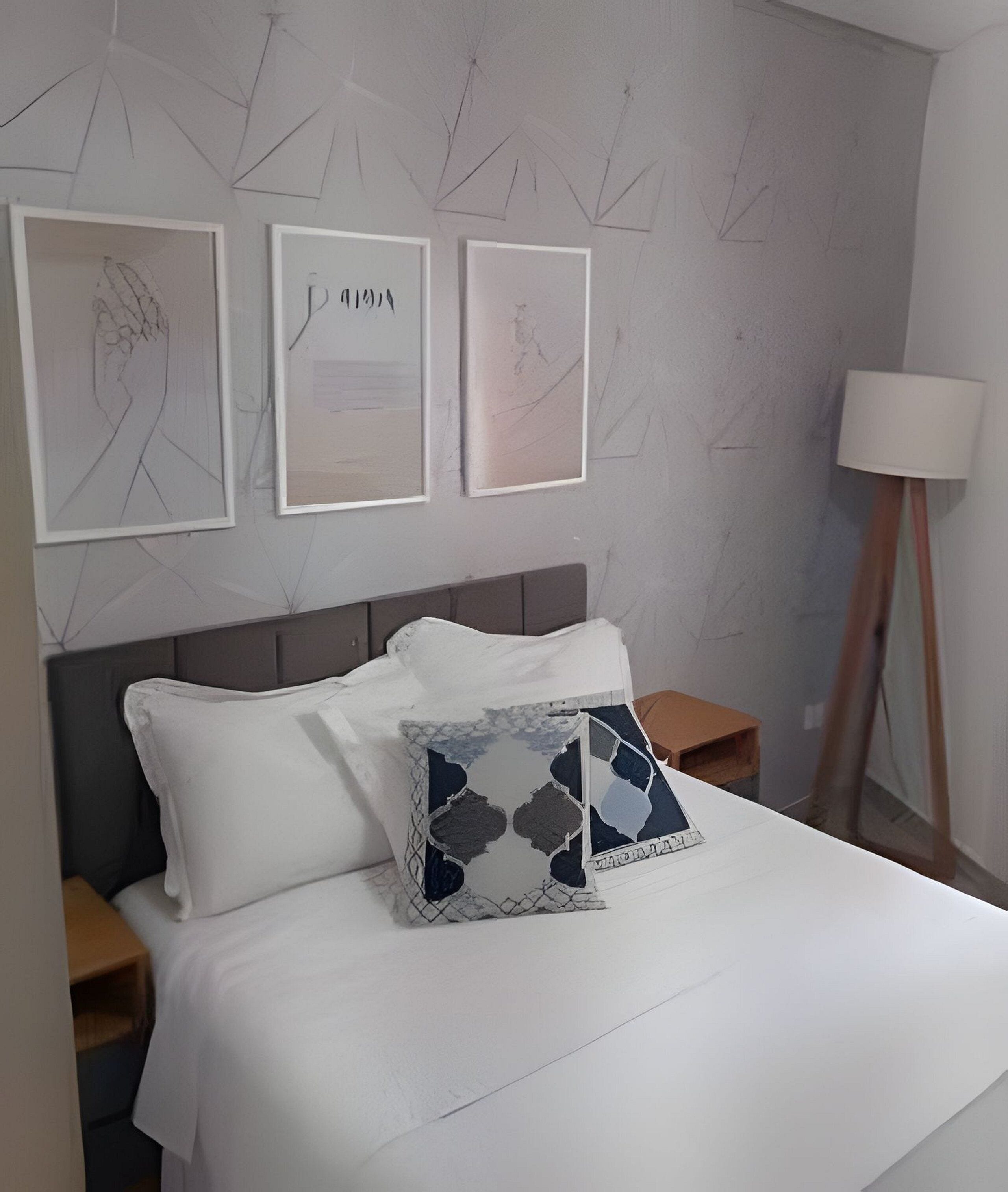 A neatly made bed with white bedding, a decorative pillow, and a wall with abstract art. There are two bedside tables and a floor lamp.