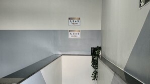 A stairwell with two sets of handrails, a wall-mounted emergency exit sign, and directional signs for apartment numbers 1, 2, 3, 4, 5, and 6. - Residencial Felicita (Barueri)