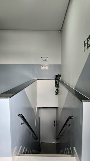 A stairwell with two sets of handrails, a wall-mounted emergency exit sign, and directional signs for apartment numbers 1, 2, 3, 4, 5, and 6.