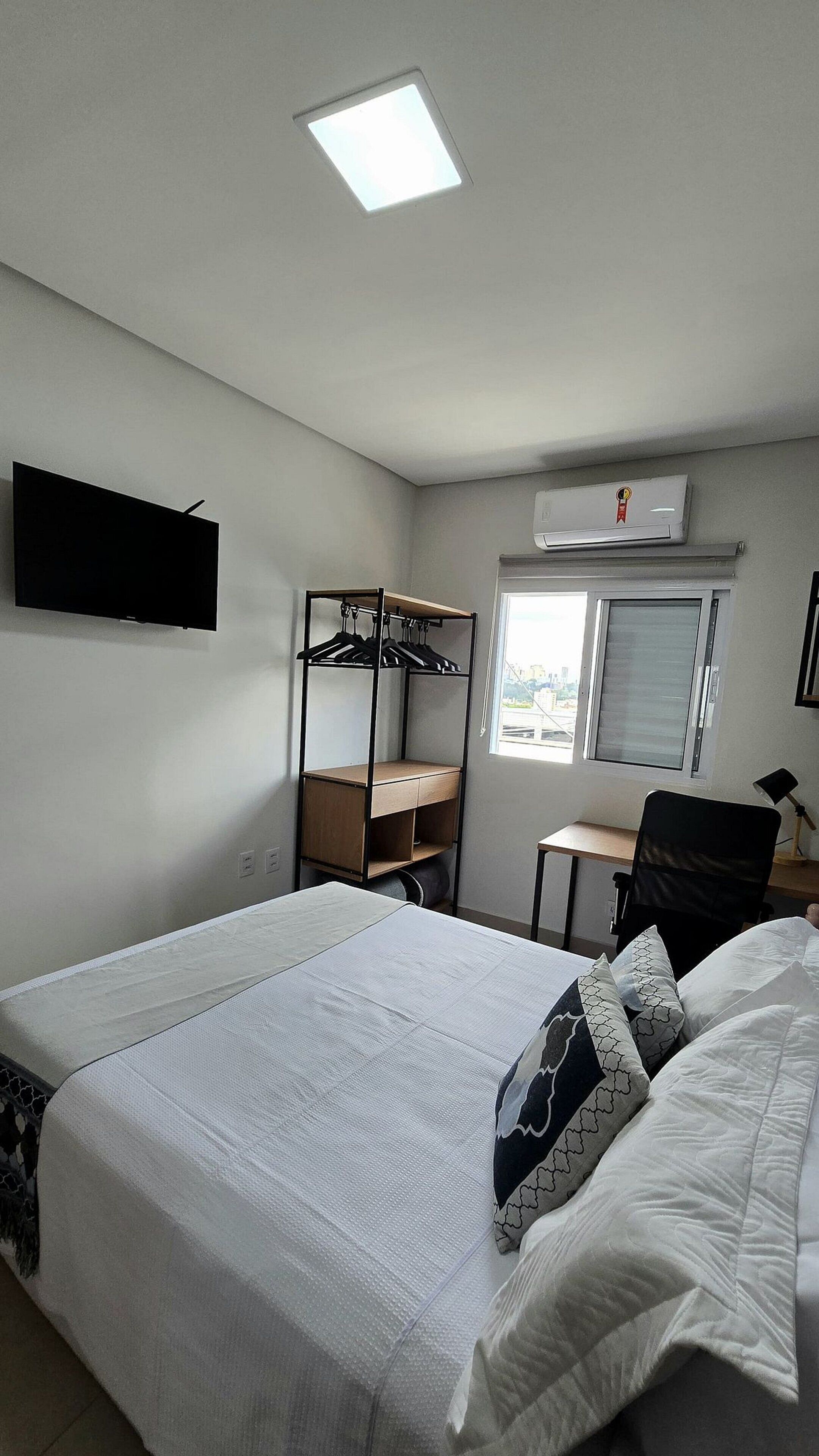 Une chambre à coucher comprenant un lit, un bureau, une chaise, une armoire, un téléviseur et un appareil de climatisation.