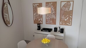 A dining area with a round table, chairs, a coffee machine, a kettle, and decorative wall panels.