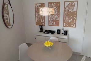 Un comedor con una mesa redonda, sillas, una cafetera, un hervidor y paneles decorativos en la pared.