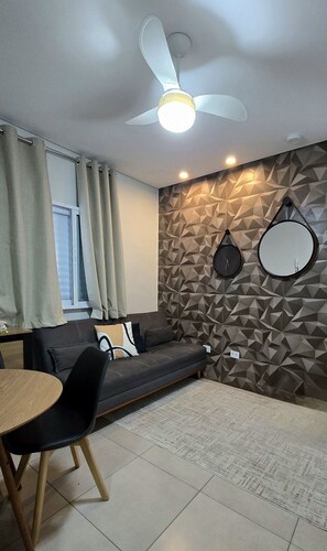 A modern living room with a sofa, a dining table, a ceiling fan, and geometric-patterned walls.
