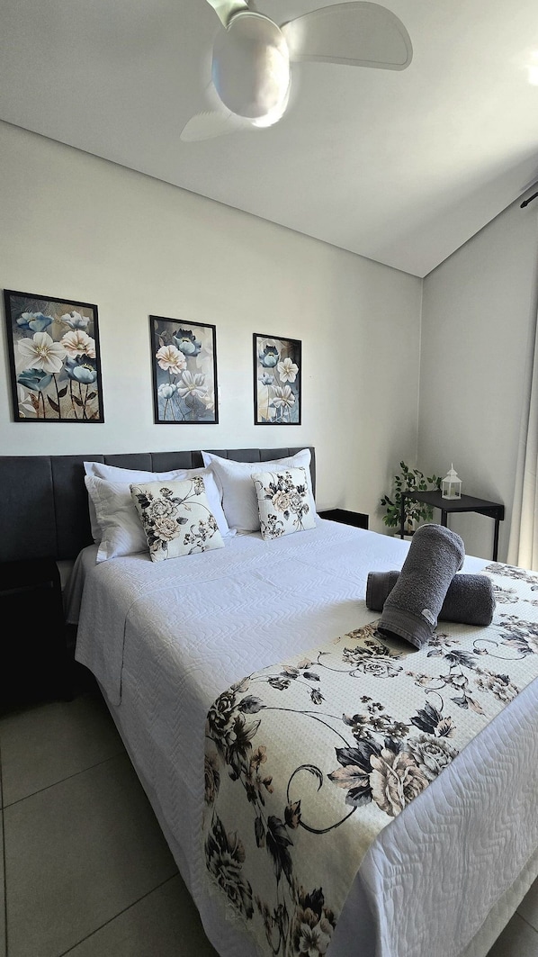 Un dormitorio con cama, ventilador de techo y tres cuadros florales.