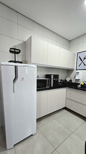 A kitchen with white cabinets, a white refrigerator, a microwave, and a sink.