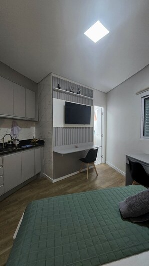 A compact kitchen with a built-in stove, a flat-screen TV, and a small seating area with a chair.