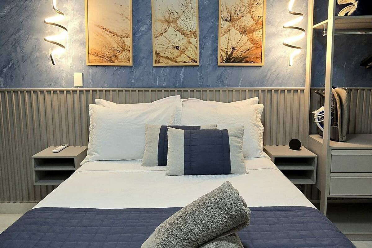 A modern bedroom with a large bed, two wall-mounted light fixtures, and three framed artworks.
