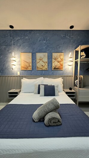 A modern bedroom with a large bed, two wall-mounted light fixtures, and three framed artworks.