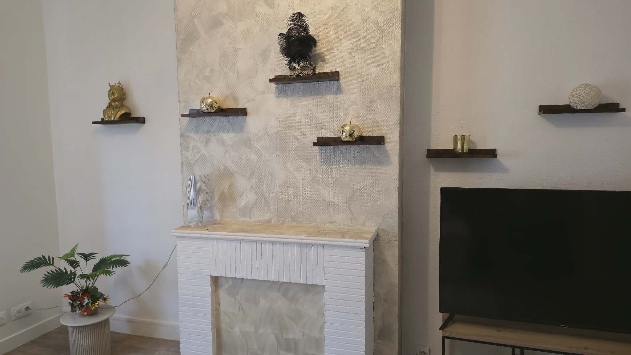 A living room with a fireplace, a TV, and decorative items on shelves.