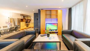 Una sala de estar moderna con un sofá, una mesa de centro, un televisor y una cocina al fondo.
