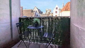 Un balcón con mesa y sillas, una planta en maceta y vistas a edificios.