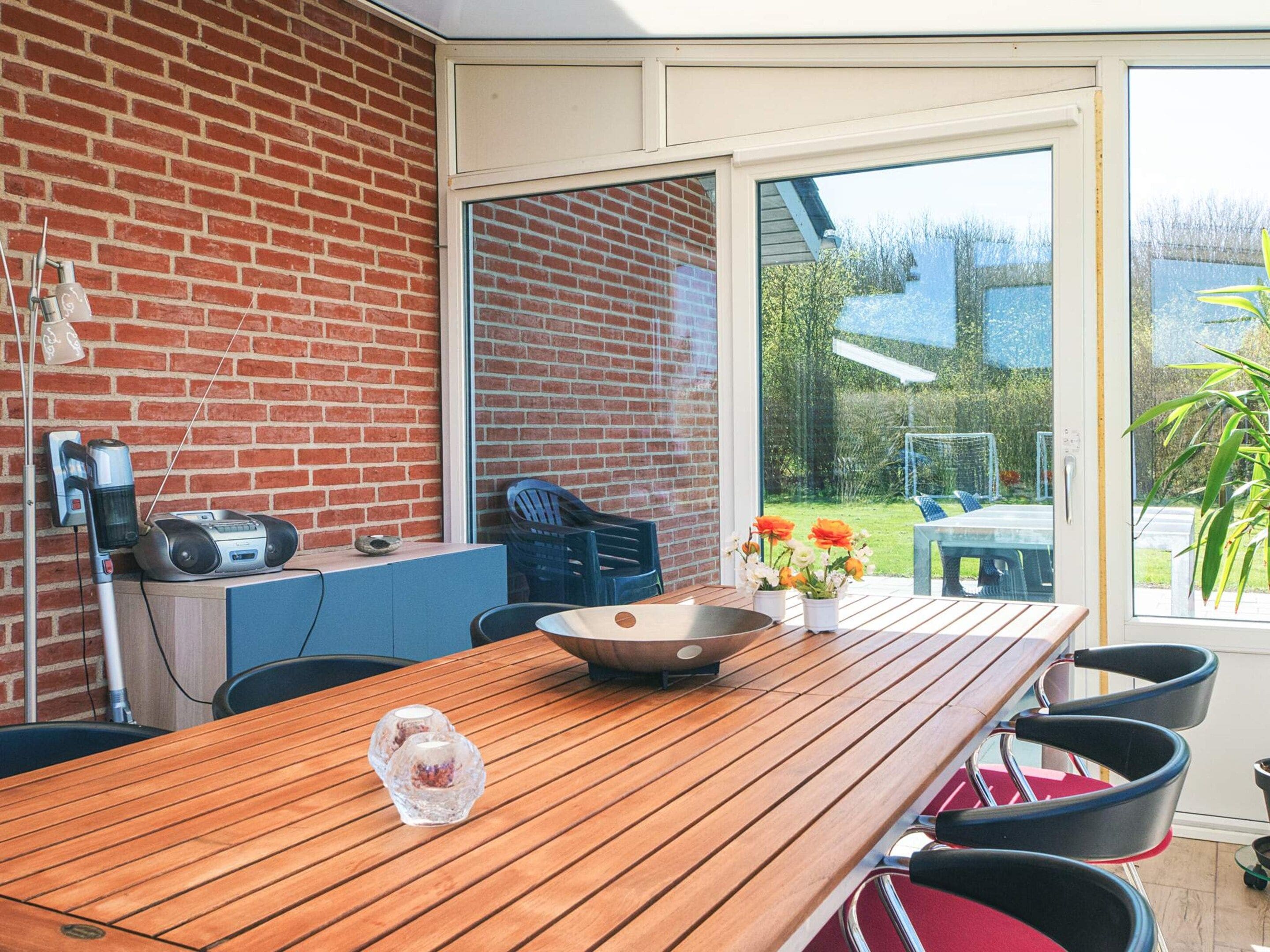 A wooden table with chairs, a brick wall, and a sliding glass door leading to a garden.