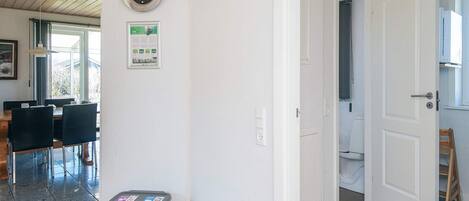 A room with a wooden ceiling, a clock on the wall, a trash bin, and a door leading to another room.