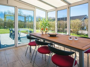 Una veranda con tavolo in legno, sedie rosse e vista su un giardino.