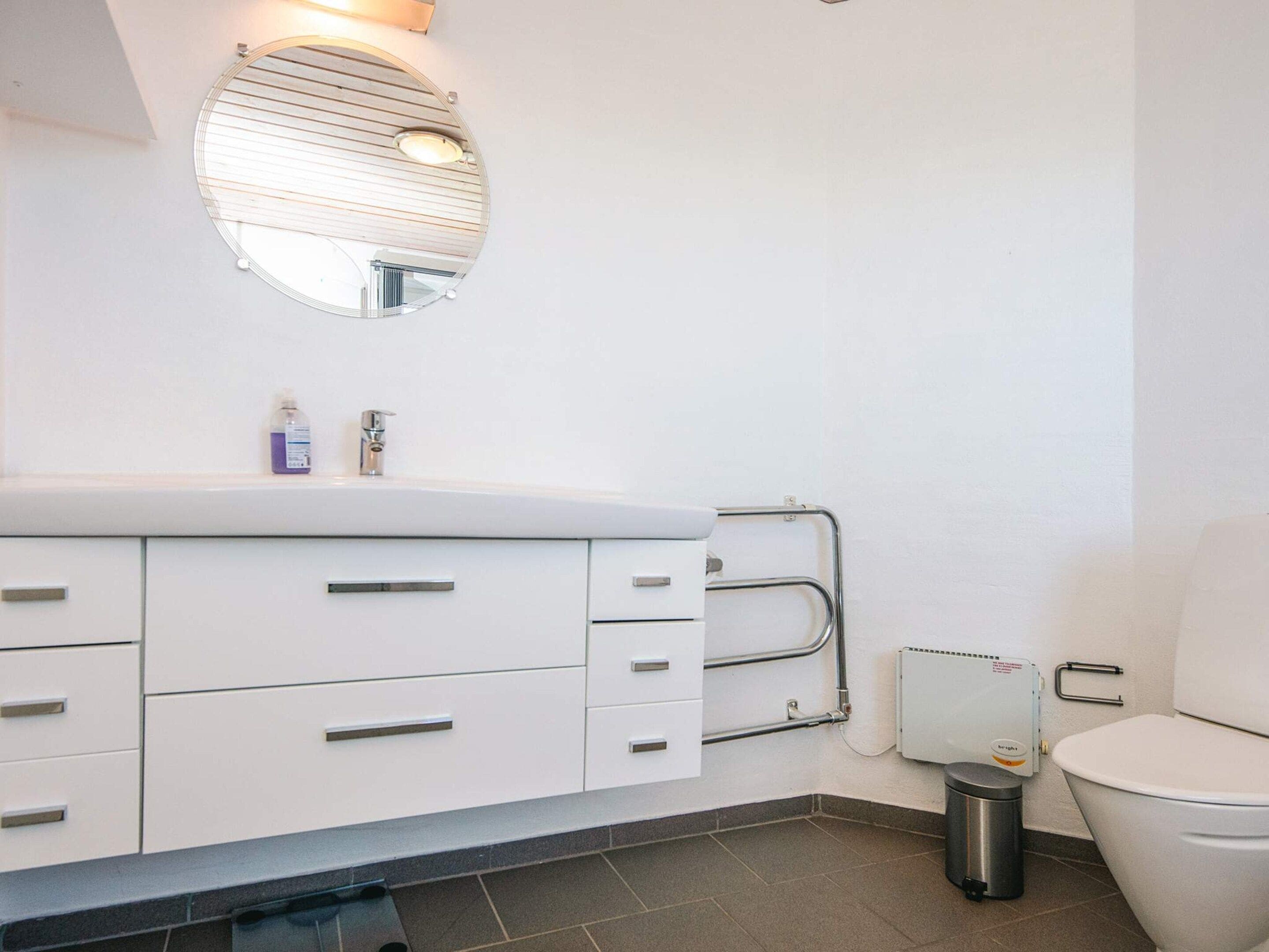 A modern bathroom with a white sink, mirror, and toilet.