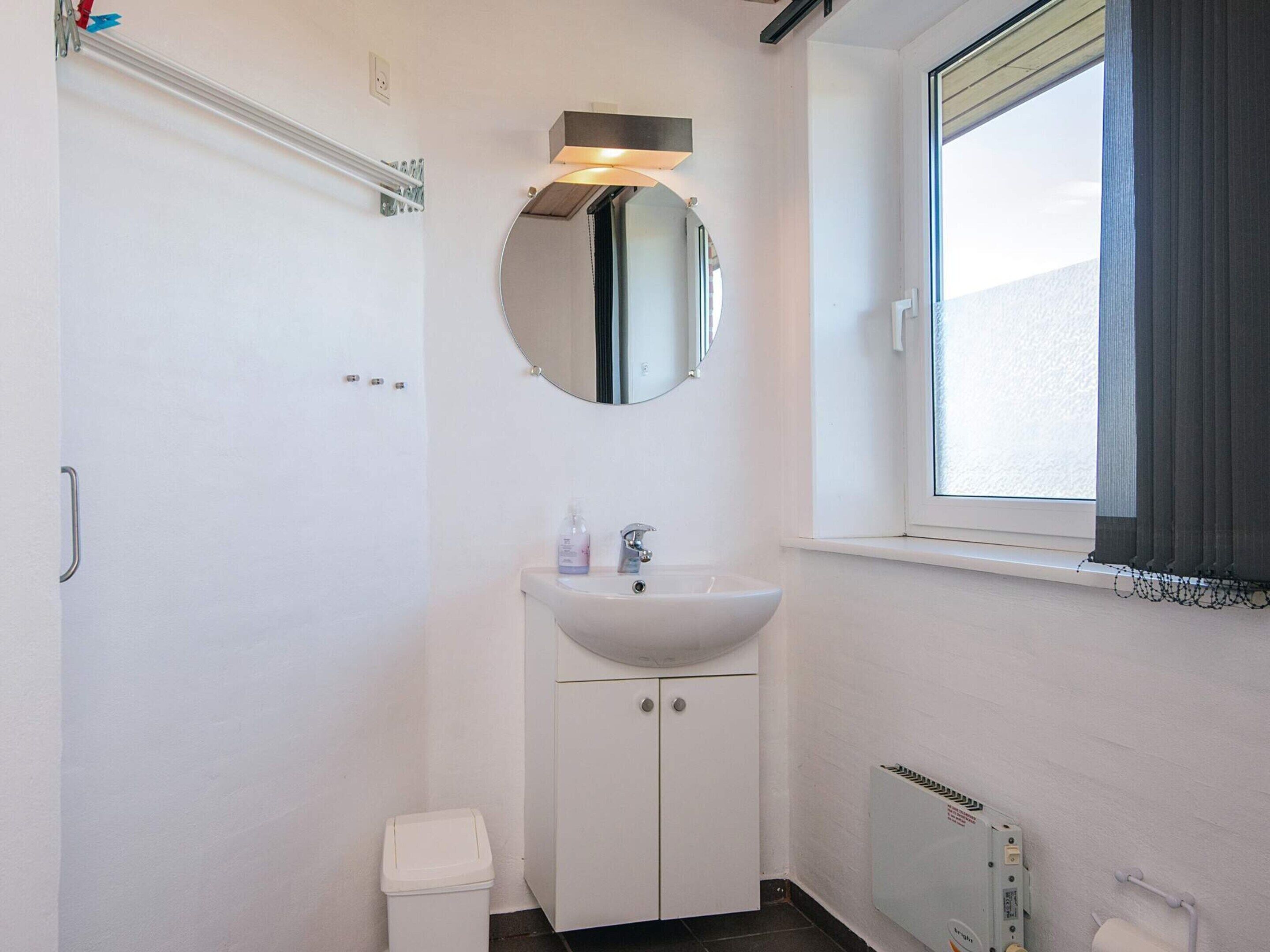 A bathroom with a white sink, a mirror, a toilet, and a window with curtains.