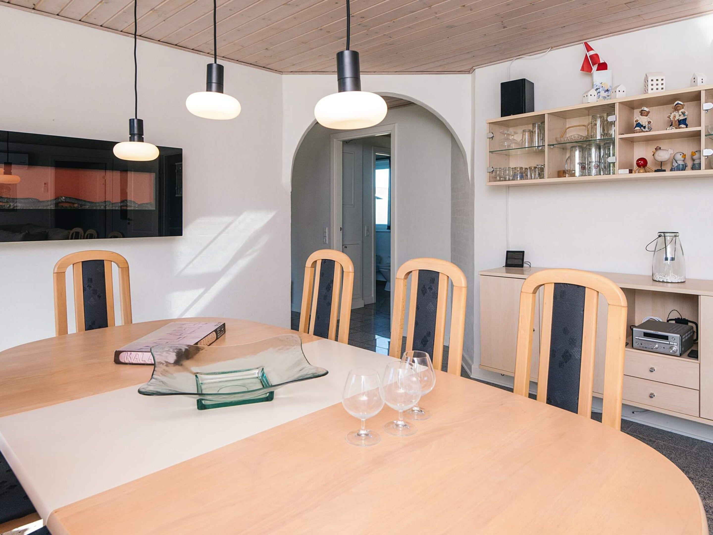 Ein Essbereich mit einem Holztisch, Stühlen und einem an der Wand befestigten Fernseher.