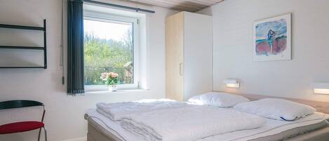 A bedroom with a bed, a window with curtains, a chair, and a painting on the wall.