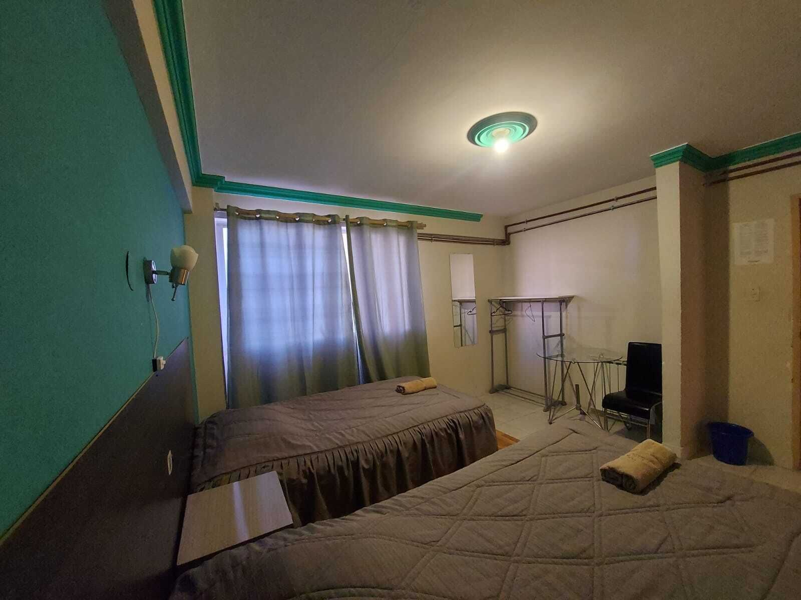Una habitación con dos camas, un escritorio, una silla, un espejo y una lámpara en el techo.