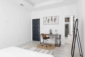 Ein Schlafzimmer mit Bett, Schreibtisch, Stuhl, einer Tür und einer Wand mit Kunstwerken.