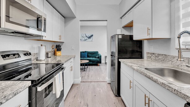 A modern kitchen with white cabinetry, a stainless steel refrigerator, and a granite countertop. - Causeway House | Coastal 2BR Stay (Bay Harbor Islands)