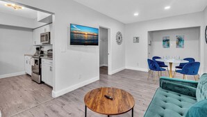 A modern living room with a teal sofa, a wooden coffee table, and a dining area with blue chairs. - Causeway House | Coastal 2BR Stay (Bay Harbor Islands)