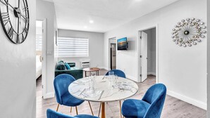 A modern dining area with a round table, blue chairs, and a wall clock. - Causeway House | Coastal 2BR Stay (Bay Harbor Islands)