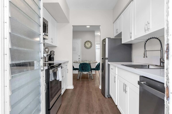 A modern kitchen with white cabinetry, stainless steel appliances, and a dining area with a teal chair. - Chic 2BR in Bay Harbor Islands near beach, shopping, and dining (Bay Harbor Islands)