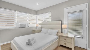 Un dormitorio moderno con una cama grande, dos mesitas de noche con lámparas y una ventana con persianas.