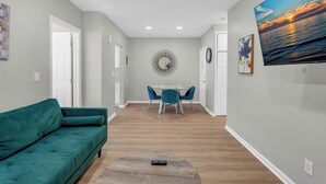 Una sala de estar moderna con un sofá color turquesa, un comedor con sillas color turquesa, una mesa redonda y un televisor grande en la pared.