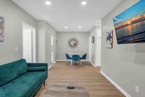 Una sala de estar moderna con un sofá color turquesa, un comedor con sillas color turquesa, una mesa redonda y un televisor grande en la pared.