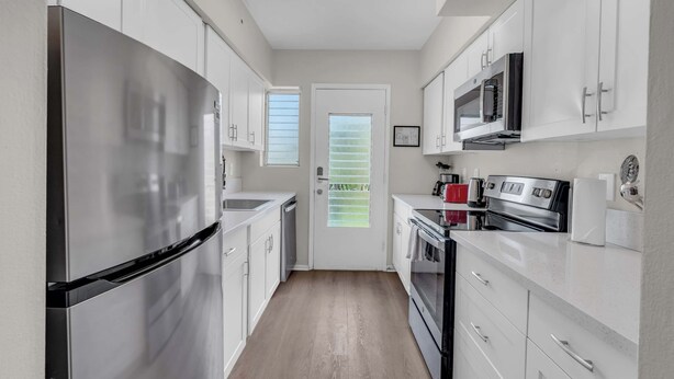 Una cocina moderna con electrodomésticos de acero inoxidable, armarios blancos y piso de madera.
