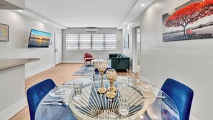 A modern dining area with a round glass table, blue chairs, and decorative glassware. - Old Bay Vista | Stylish 1BR Getaway (Bay Harbor Islands)