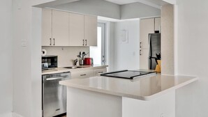 A modern kitchen with white cabinets, a stainless steel dishwasher, a microwave, and a red coffee maker. - Old Bay Vista | Stylish 1BR Getaway (Bay Harbor Islands)