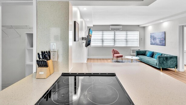 A modern kitchen with a built-in stove, a dining area with a round table, and a teal sofa. - Old Bay Vista | Stylish 1BR Getaway (Bay Harbor Islands)