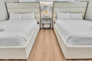 Una habitación de hotel con dos camas, una mesita de noche con lámpara y suelo de madera.