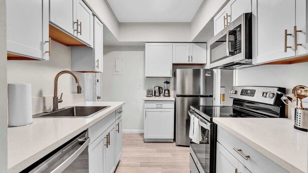 Una cucina moderna con mobili bianchi, elettrodomestici in acciaio inossidabile e un piano di lavoro in legno.