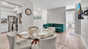 Una cucina moderna con elettrodomestici in acciaio inossidabile, un'area pranzo con tavolo in vetro e un divano verde in un soggiorno.