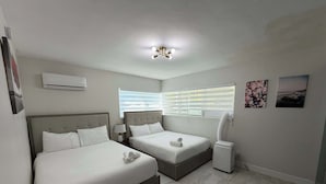 Une chambre d’hôtel avec deux lits, un luminaire au plafond, un climatiseur, une fenêtre avec des stores et un climatiseur fixé au mur.