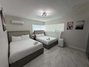 A hotel room with two beds, a ceiling light, an air conditioner, a window with blinds, and a wall-mounted air conditioner. - Modern 2BR in Bay Harbor Islands close to beach, shops, and dining (Bay Harbor Islands)