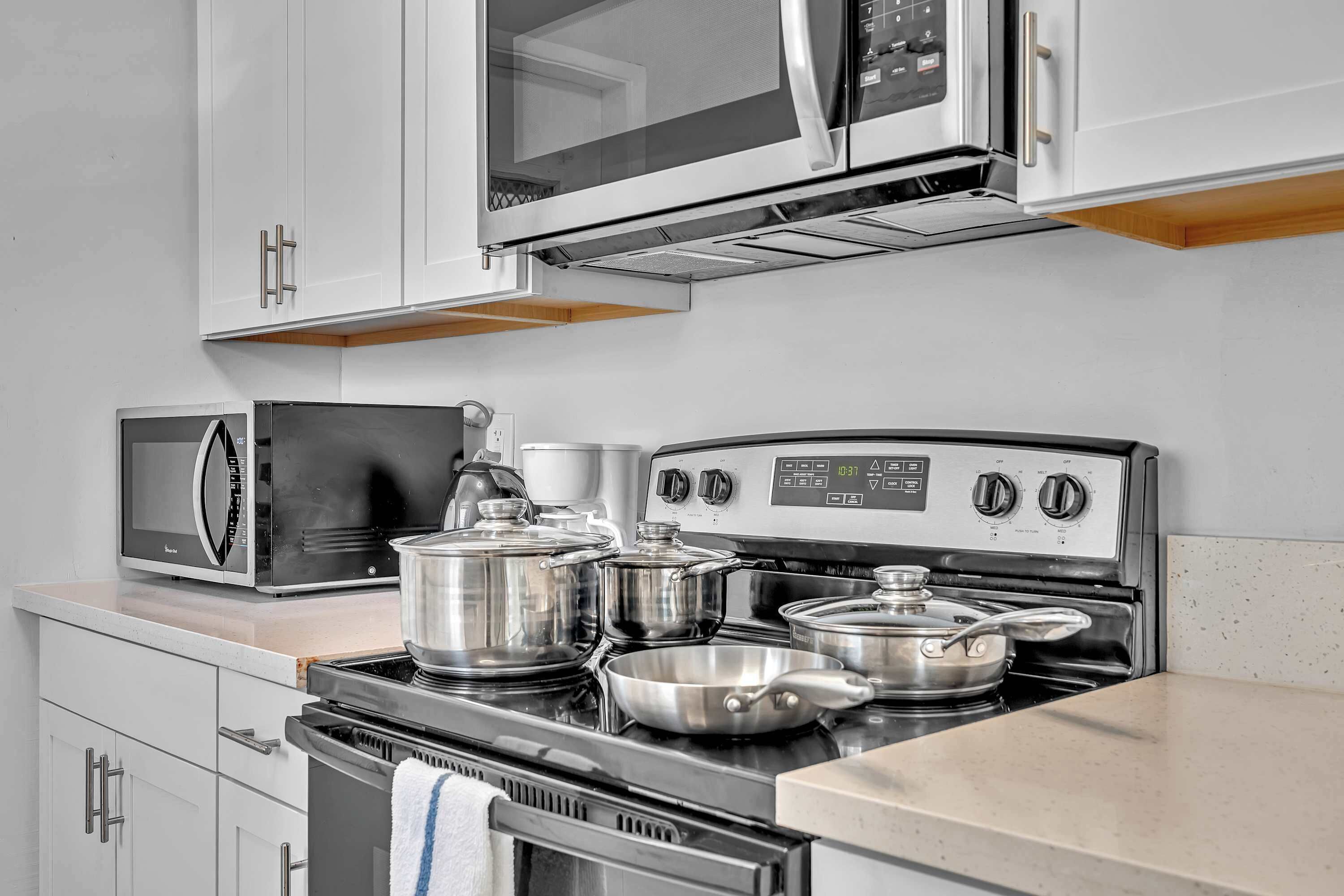 A kitchen with a microwave, stove, pots, and a coffee maker.
