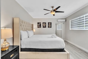 Habitación de hotel con cama, ventilador de techo, mesita de noche, lámpara y cuadros en la pared.