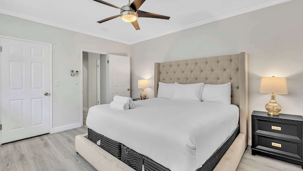 Une chambre à coucher avec un lit, un ventilateur de plafond, une table de chevet et une porte.