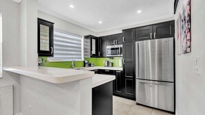 Une cuisine moderne avec un îlot central blanc, des meubles noirs, des appareils électroménagers en acier inoxydable et un pare-feu vert.