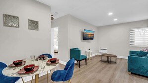 A modern living room with a dining area, teal sofas, a flat-screen TV, and a fireplace. - Boutique 2BR in Bay Harbor Islands close to beach, shops, and dining (Bay Harbor Islands)